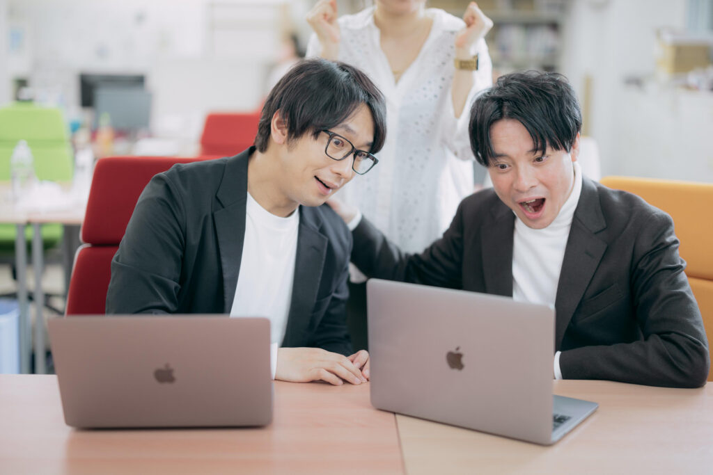 ノートパソコンを見て利益アップに喜ぶ男性2人の画像